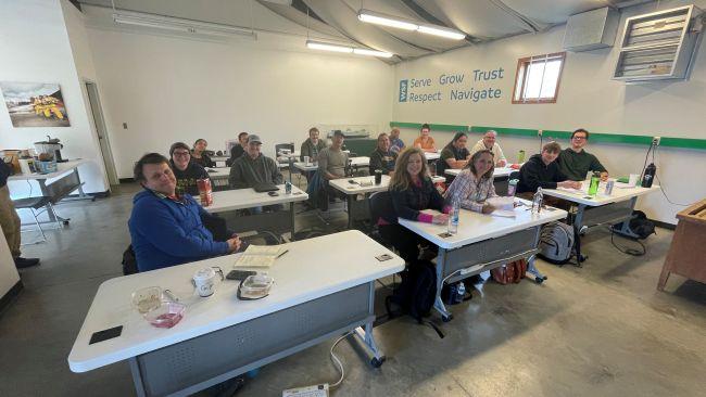People seated in a classroom setting with tables and motivational words on the wall