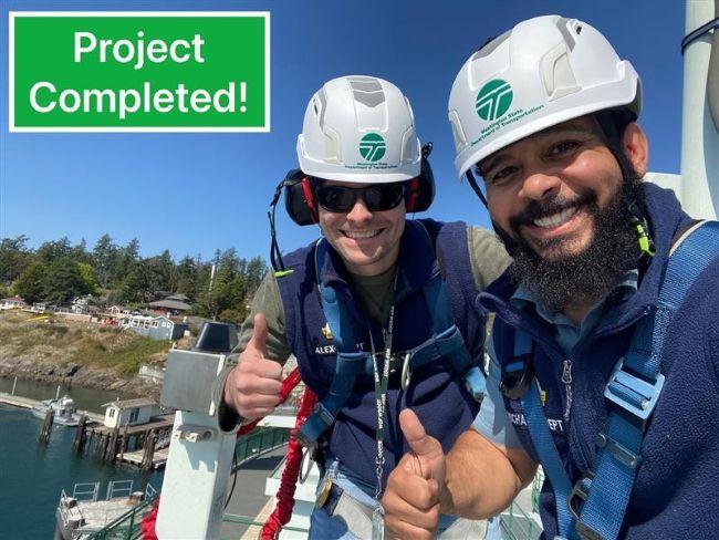 Two individuals in safety gear giving thumbs up with a coastal scene in the background; text reads "Project Completed!"