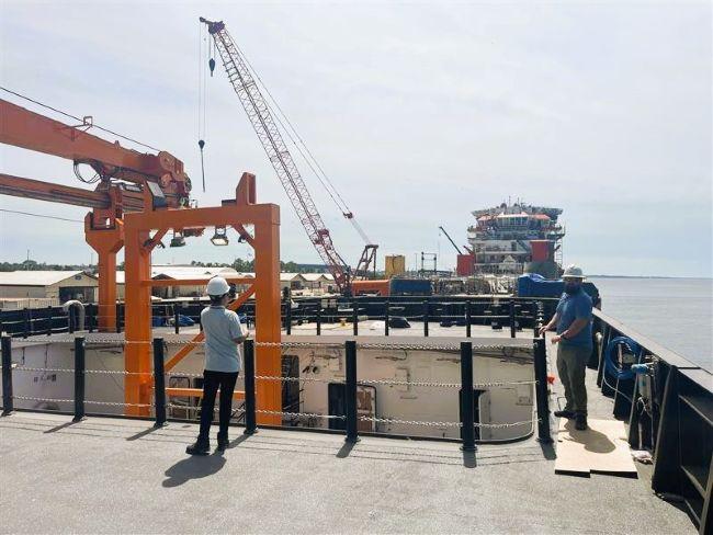 Two workers on a vessel deck with industrial equipment and cranes.