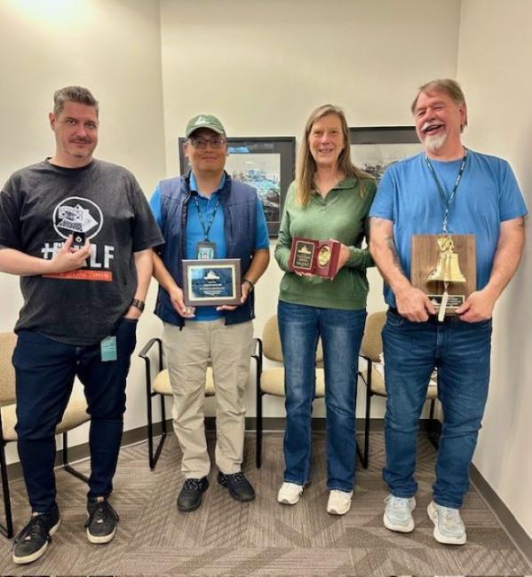 Four people standing with awards in a room.