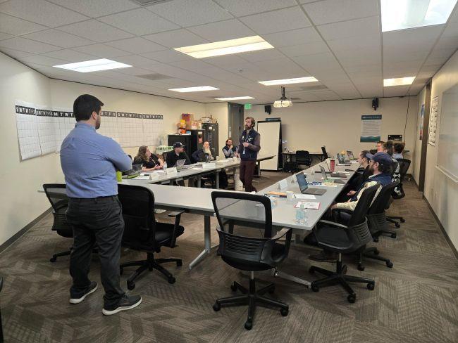 A conference room with people seated around a U-shaped table during a meeting.